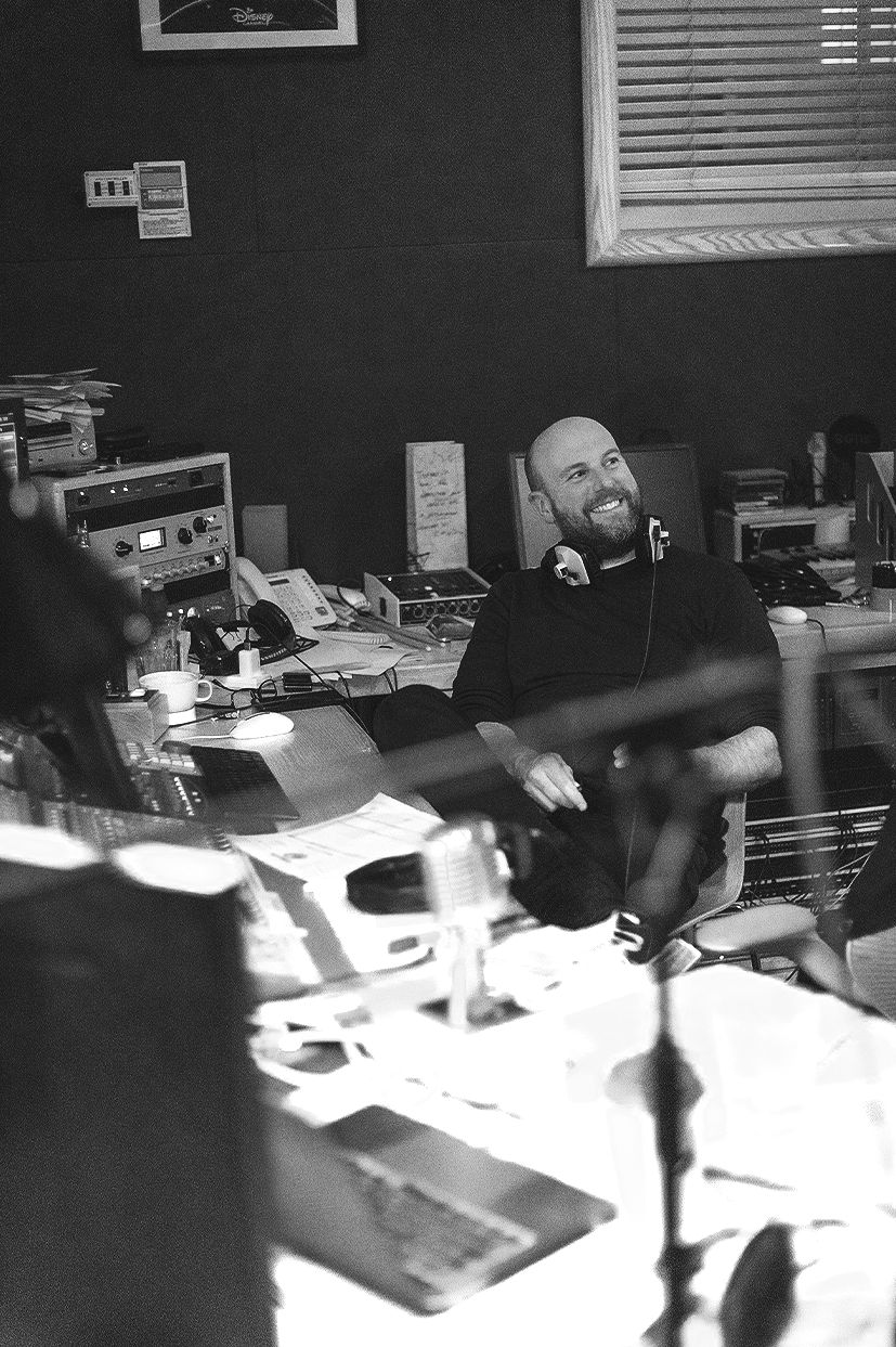 Black-and-white candid photograph of Dom Boucher working at a studio mixing desk during a radio drama session.